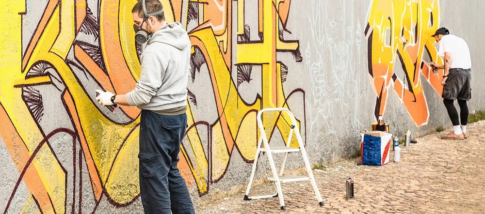 Zwei junge Männer sprühen ein Graffito auf eine Wand in Berlin